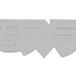 Puede incluir: Un objeto tridimensional de color gris claro que presenta los caracteres katakana japoneses para Mosura, que se traduce como Mothra. El diseño es una pieza sólida de cara plana con letras en relieve y un pequeño orificio circular a la derecha.