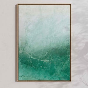 May include: Abstract art print in a wooden frame. The artwork features a gradient of colors, transitioning from white to shades of teal and deep green. The textured surface gives the piece a weathered appearance, evoking a sense of the ocean.