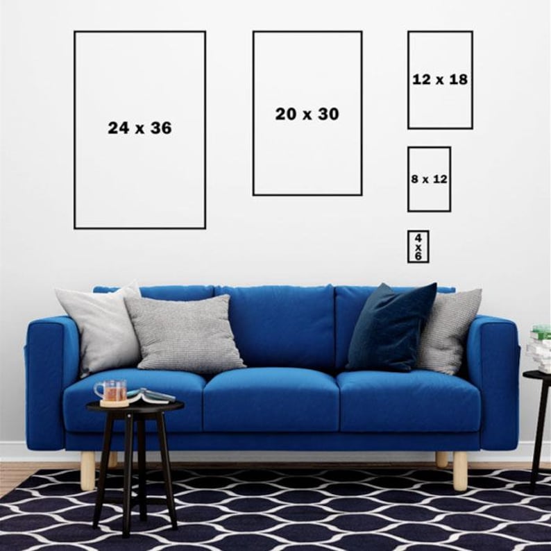 Op de afbeelding: Een blauwe bank met drie kussens en een zwarte bijzettafel met een boek en een kopje erop. Er hangen vijf ingelijste foto's aan de muur achter de bank. De foto's zijn van verschillende groottes en hebben zwarte lijsten. De foto's hebben de volgende afmetingen: 61 x 91 cm, 51 x 76 cm, 30 x 46 cm, 20 x 30 cm en 10 x 15 cm.