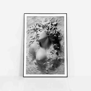 May include: Black and white photograph of a sculpted woman's head and bust, with flowers and leaves in her hair, lying on a textured surface.