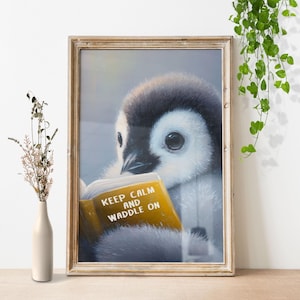 Może przedstawiać: Oprawiony wydruk przedstawiający małego pingwina czytającego książkę. Pingwin jest czarny, biały i szary, z dużymi oczami i puszystymi piórami. Książka jest żółta z napisem "KEEP CALM AND WADDLE ON". Rama jest w kolorze jasnobrązowym.