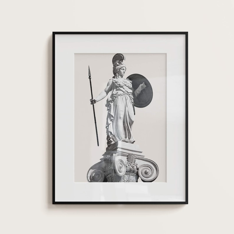 Op de afbeelding: Zwart-witfoto van een standbeeld van een vrouw die een speer en een schild vasthoudt. Het standbeeld staat op een voetstuk met sierlijke details. Het standbeeld is ingelijst in een zwart frame.