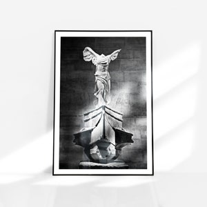 Puede incluir: Fotografía en blanco y negro de una estatua de la Victoria Alada de Samotracia, una escultura griega, de pie sobre un pedestal. La estatua está en un entorno museístico.