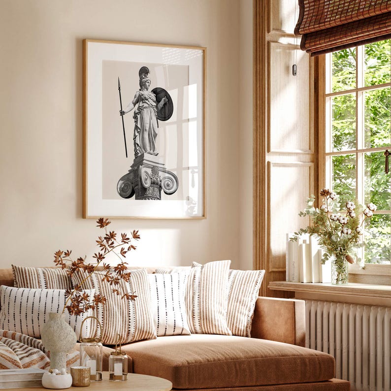 Op de afbeelding: Een zwart-witfoto van een standbeeld van een vrouw die een speer en een schild vasthoudt. Het standbeeld staat op een kolom met ingewikkelde houtsnijwerk. De foto is ingelijst in een licht houten lijst en hangt aan een beige muur.