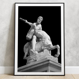 May include: Black and white photograph of a marble statue of a man wrestling a centaur. The statue is set against a black background.