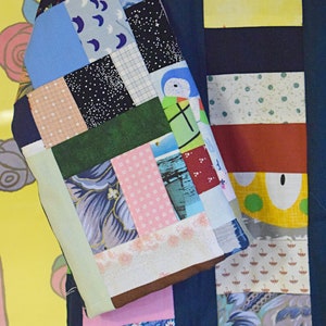 Puede incluir: Una tela de patchwork azul y blanca con una variedad de patrones, que incluyen lunares, rayas y dise&ntilde;os florales. La tela est&aacute; cosida en un patr&oacute;n de cuadr&iacute;cula y tiene un borde verde claro.