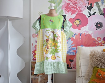 May include: A green, yellow, and white patchwork dress with a floral print and a ruffled hem. The dress is on a white mannequin against a floral wallpaper background.