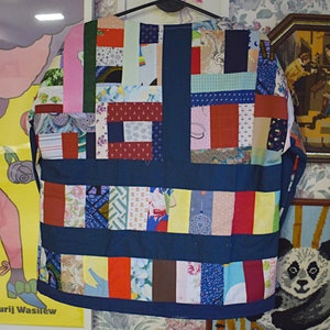 Puede incluir: Una camisa azul de patchwork con una variedad de telas y patrones coloridos. La camisa est&aacute; colgada de una percha y tiene una forma cuadrada.