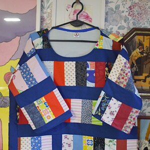 Puede incluir: Una blusa azul de patchwork con cuello redondo y mangas largas. La blusa est&aacute; hecha de diferentes telas de colores, incluyendo rojo, blanco, azul y verde. Las mangas tambi&eacute;n son de patchwork y tienen una base azul con rayas rojas, blancas y verdes.