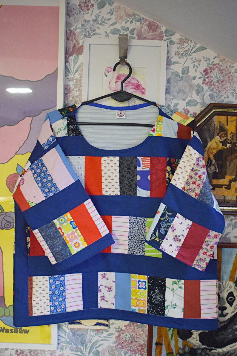 Puede incluir: Una blusa azul de patchwork con cuello redondo y mangas largas. La blusa est&aacute; hecha de diferentes telas de colores, incluyendo rojo, blanco, azul y verde. Las mangas tambi&eacute;n son de patchwork y tienen una base azul con rayas rojas, blancas y verdes.