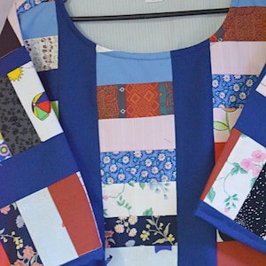 May include: A blue patchwork shirt with a variety of colorful fabric squares. The shirt has a round neckline and short sleeves. The fabric squares feature floral patterns, geometric designs, and stripes.