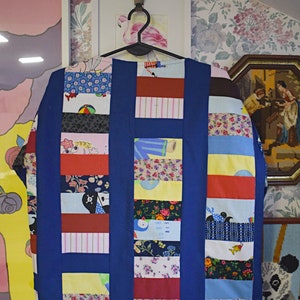 May include: A blue patchwork jacket with a variety of colorful fabric squares. The jacket has a collar and long sleeves. The fabric squares feature different patterns, including floral, geometric, and cartoon characters.