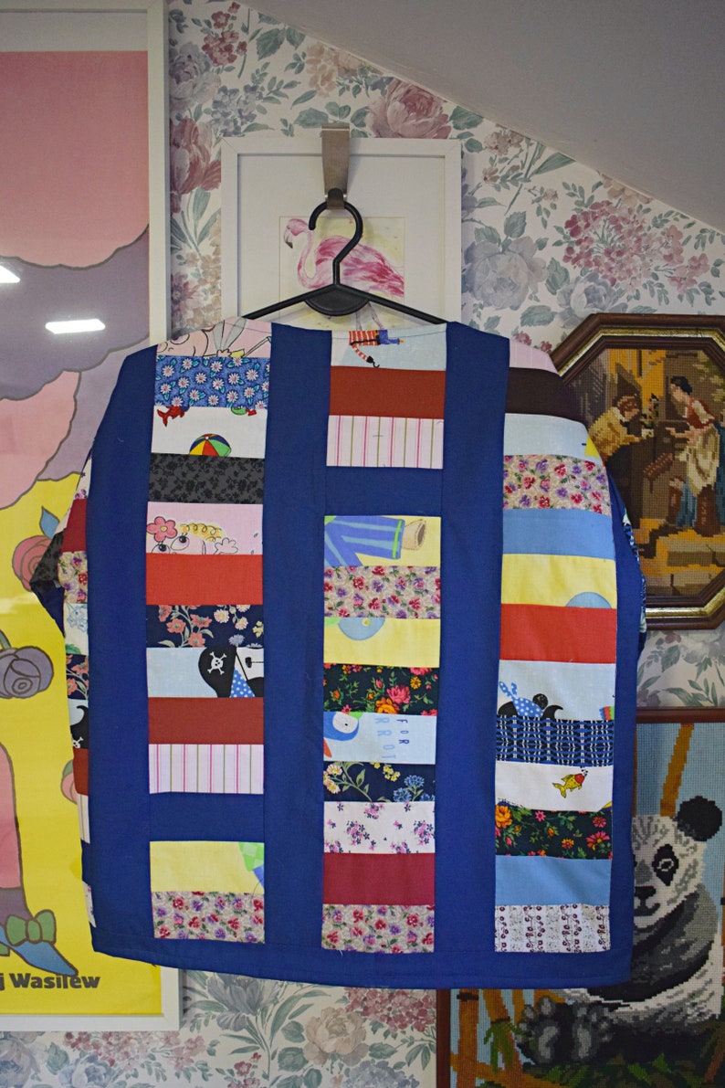 May include: A blue patchwork jacket with a variety of colorful fabric squares. The jacket has a collar and long sleeves. The fabric squares feature different patterns, including floral, geometric, and cartoon characters.