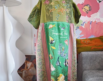 Puede incluir: Vestido patchwork verde y rosa con un diseño de peces tropicales. El vestido tiene cuello redondo, mangas cortas y bajo con volantes. El panel frontal muestra el texto "Tropical Fish Australia" con ilustraciones de peces.