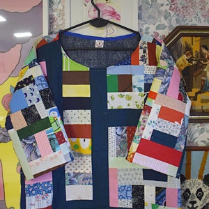 Puede incluir: Una camisa azul de patchwork con una variedad de cuadrados de tela de colores. La camisa tiene un cuello redondo y mangas tres cuartos. Los cuadrados de tela est&aacute;n dispuestos en un patr&oacute;n horizontal.