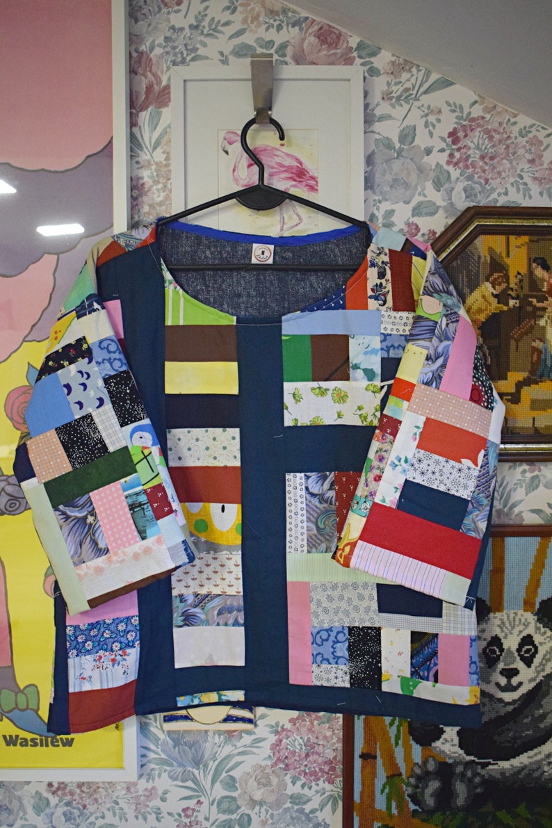 Puede incluir: Una camisa azul de patchwork con una variedad de cuadrados de tela de colores. La camisa tiene un cuello redondo y mangas tres cuartos. Los cuadrados de tela est&aacute;n dispuestos en un patr&oacute;n horizontal.