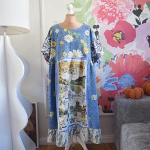Könnte beinhalten: Ein knielanges Kleid aus blauem Stoff mit weißem Gänseblümchenmuster, kurzen Ärmeln mit dunkelblau-weißem Blumenmuster und einem Mittelteil, das eine illustrierte Karte im Vintage-Stil mit dem Text Isle of Wight Village zeigt.