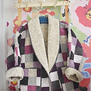 May include: A patchwork quilted jacket with a cream colored collar and a floral pattern. The jacket is hanging on a wooden ladder with a floral wallpaper background.
