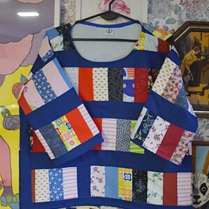 Puede incluir: Una blusa azul de patchwork con cuello redondo y mangas 3/4. La blusa est&aacute; hecha de varias telas coloridas, incluyendo estampados florales, rayas y lisas. Las mangas tambi&eacute;n son de patchwork y tienen un ribete azul contrastante.
