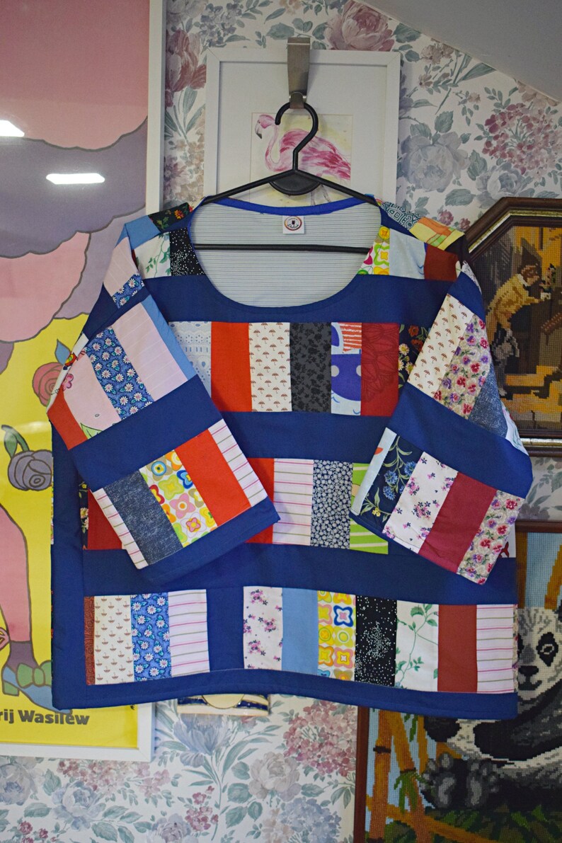 Puede incluir: Una blusa azul de patchwork con cuello redondo y mangas 3/4. La blusa est&aacute; hecha de varias telas coloridas, incluyendo estampados florales, rayas y lisas. Las mangas tambi&eacute;n son de patchwork y tienen un ribete azul contrastante.