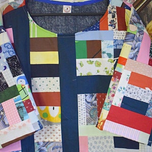 Puede incluir: Una camisa azul de patchwork con una variedad de cuadrados de tela de colores. La camisa tiene un cuello redondo y mangas cortas.