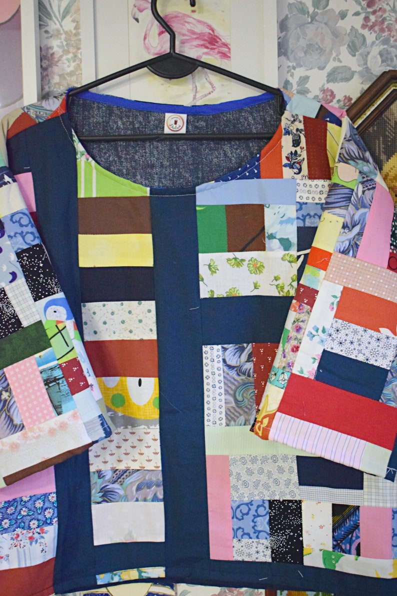 Puede incluir: Una camisa azul de patchwork con una variedad de cuadrados de tela de colores. La camisa tiene un cuello redondo y mangas cortas.