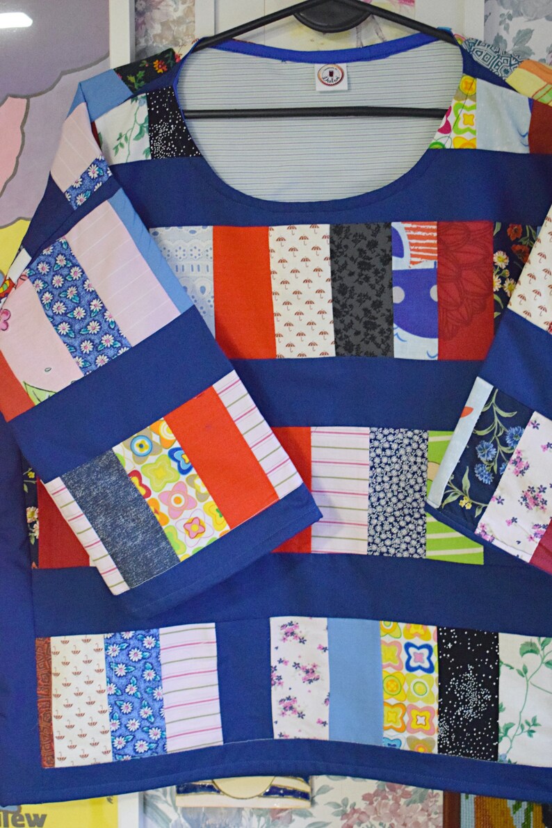 Puede incluir: Una camisa azul de patchwork con una variedad de telas coloridas cosidas juntas en un patr&oacute;n de rayas. La camisa tiene un cuello redondo y mangas largas.
