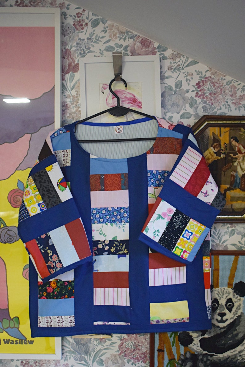 May include: A blue patchwork top with a variety of colorful fabrics, including floral prints, stripes, and geometric patterns. The top has a round neckline and three-quarter sleeves.