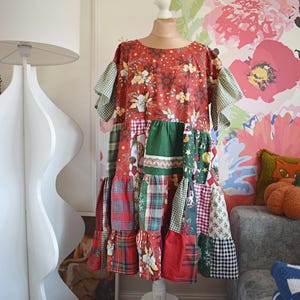Pode incluir: Vestido patchwork em manequim. O vestido apresenta um top vermelho com estampa floral, xadrez verde e vermelho e vários tecidos estampados na saia. Possui mangas curtas com acabamento em vichy verde e bainha com babados.