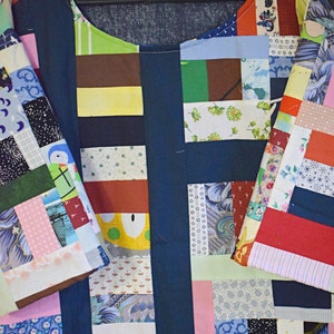 Puede incluir: Una camisa azul oscuro de patchwork con una variedad de cuadrados de tela de colores. La camisa tiene un cuello redondo y mangas cortas. Los cuadrados de tela est&aacute;n dispuestos en un patr&oacute;n horizontal.