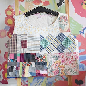 Könnte beinhalten: Eine ärmellose Patchwork-Weste aus verschiedenen Stoffen, darunter karierter Stoff, Blumenmuster und Streifen. Die Weste hängt an einem Holzbügel vor einer bunten, floralen Tapete.