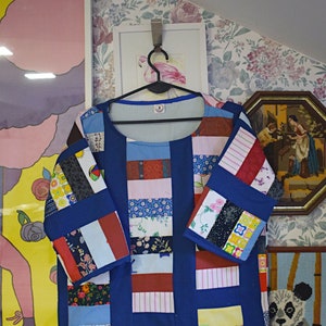 May include: A blue patchwork shirt with long sleeves and a round neckline. The shirt is made of different fabrics and patterns, including floral, striped, and geometric designs.
