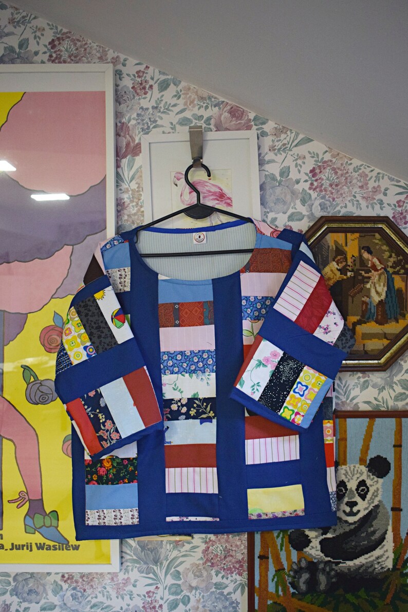 May include: A blue patchwork shirt with long sleeves and a round neckline. The shirt is made of different fabrics and patterns, including floral, striped, and geometric designs.