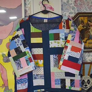 Puede incluir: Una camisa azul de patchwork con una variedad de cuadrados de tela de colores. La camisa tiene un cuello redondo y mangas cortas. Los cuadrados de tela est&aacute;n dispuestos en un patr&oacute;n de cuadr&iacute;cula.