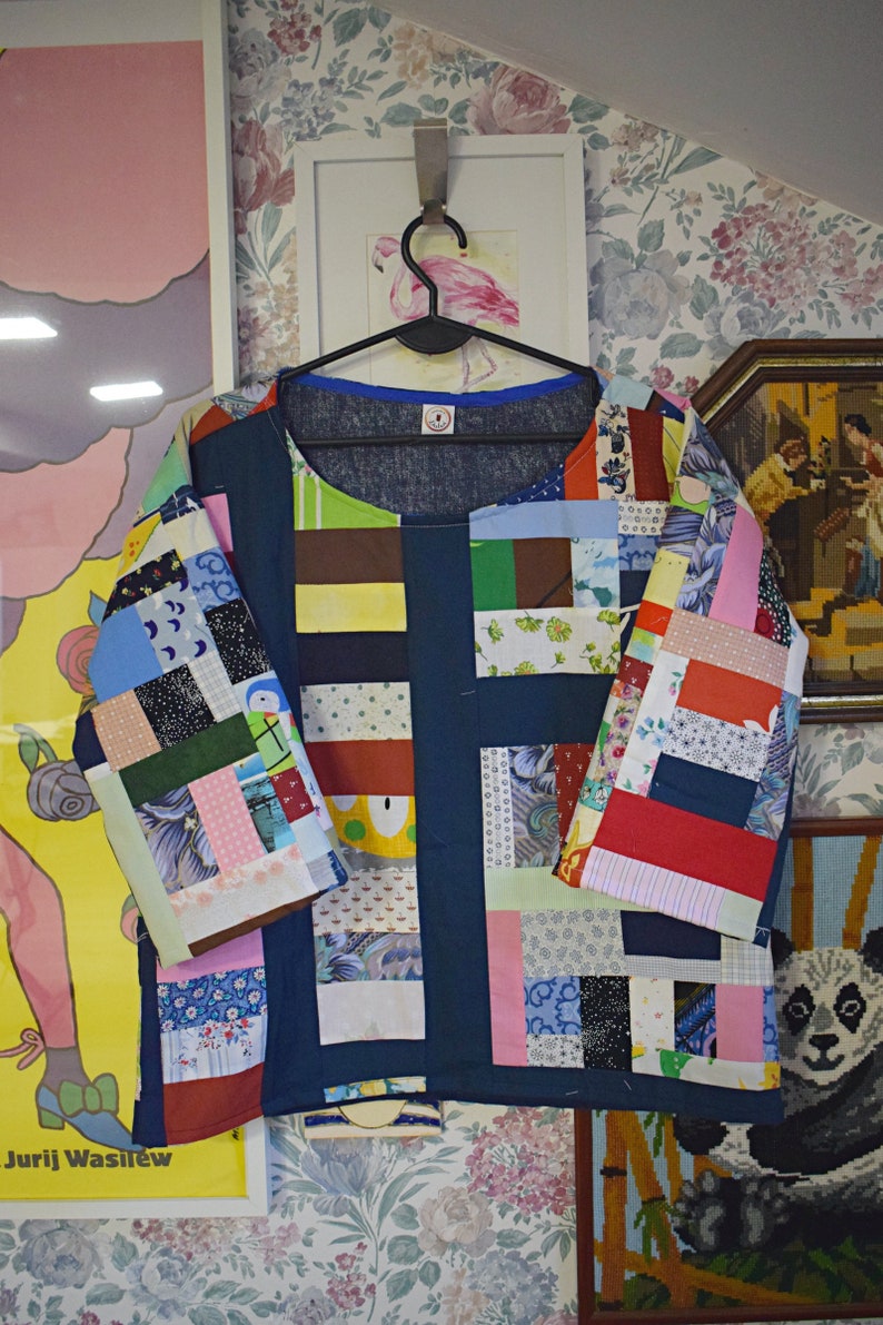 Puede incluir: Una camisa azul de patchwork con una variedad de cuadrados de tela de colores. La camisa tiene un cuello redondo y mangas cortas. Los cuadrados de tela est&aacute;n dispuestos en un patr&oacute;n de cuadr&iacute;cula.
