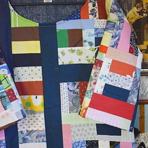 Puede incluir: Una camisa azul de patchwork con una variedad de cuadrados de tela de colores. La camisa tiene un cuello redondo y mangas cortas. Los cuadrados de tela est&aacute;n cosidos juntos en un patr&oacute;n aleatorio, creando un dise&ntilde;o &uacute;nico y llamativo.
