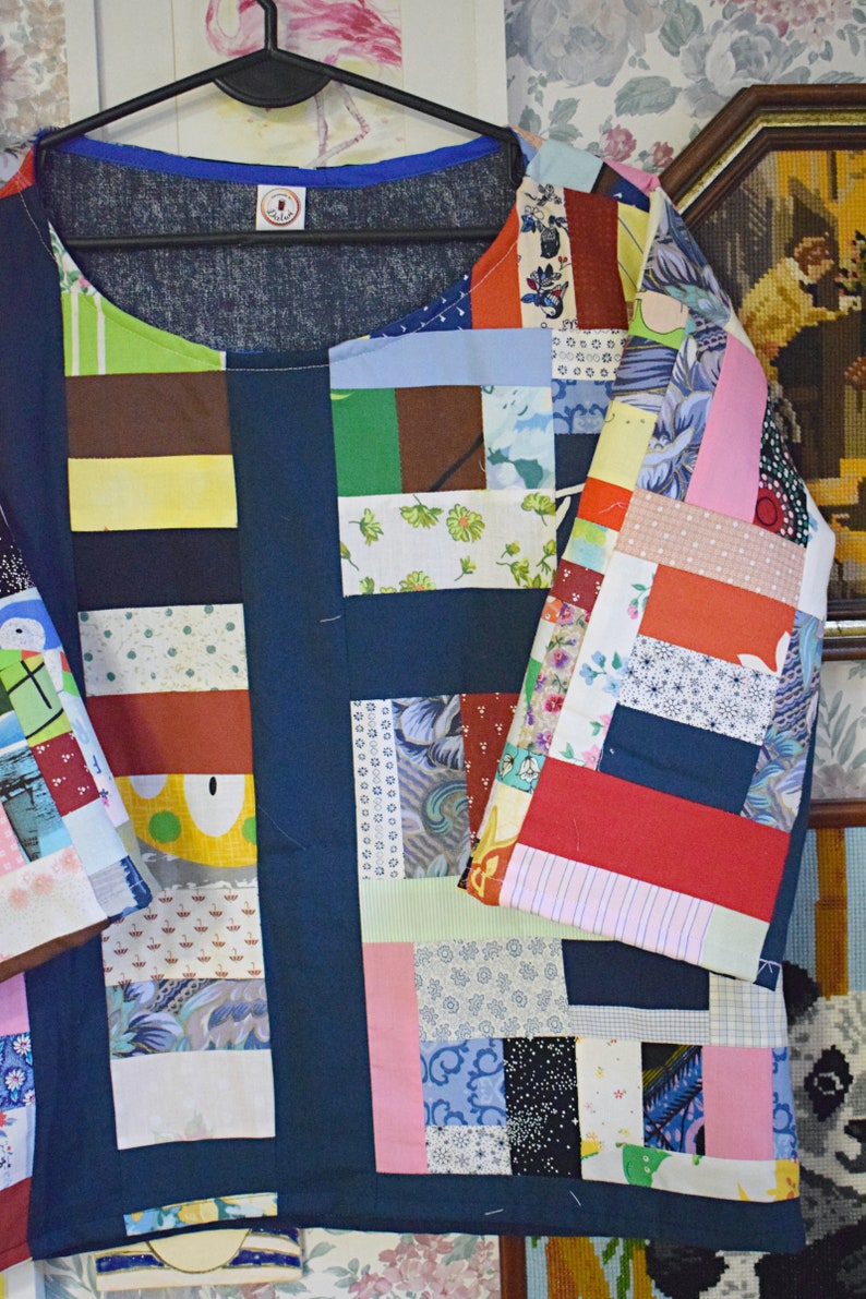Puede incluir: Una camisa azul de patchwork con una variedad de cuadrados de tela de colores. La camisa tiene un cuello redondo y mangas cortas. Los cuadrados de tela est&aacute;n cosidos juntos en un patr&oacute;n aleatorio, creando un dise&ntilde;o &uacute;nico y llamativo.