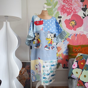 Könnte beinhalten: Ein Patchwork-Kleid mit Mickey Mouse und anderen Zeichentrickfiguren. Das Kleid hat eine blaue Basis mit verschiedenen gemusterten Paneelen, darunter Sterne, Autos und ein rot-weißer Abschnitt. Das Kleid wird auf einer Schaufensterpuppe präsentiert.