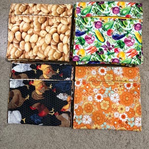 May include: Four square fabric pouches with distinct patterns: one with a brown potato print, one with a colorful vegetable print, one with a black background featuring roosters, and one with an orange and yellow floral pattern.