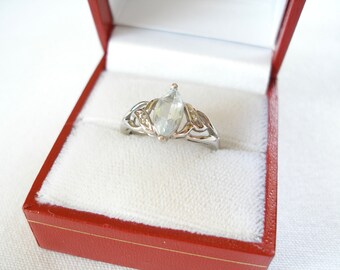 May include: A silver ring with a marquise-shaped clear gemstone and two smaller clear gemstones on the band. The ring is in a red velvet ring box.