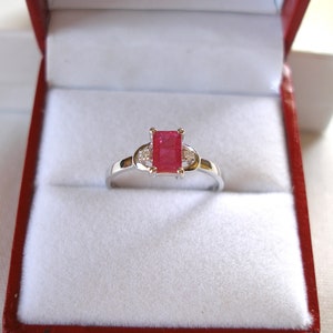 May include: A silver ring featuring a red square-shaped gemstone and two smaller clear gemstones on the band.