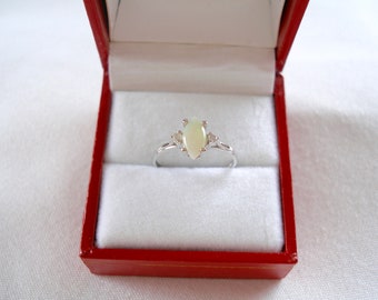 May include: A silver ring with a marquise-cut opal center stone and two smaller accent stones. The ring is displayed inside a red jewelry box with a white interior. The opal has a creamy, off-white color.