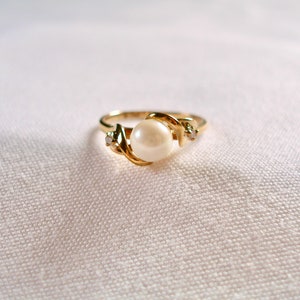 May include: A gold ring with a single pearl and two small diamonds. The ring is set in a twisted band.