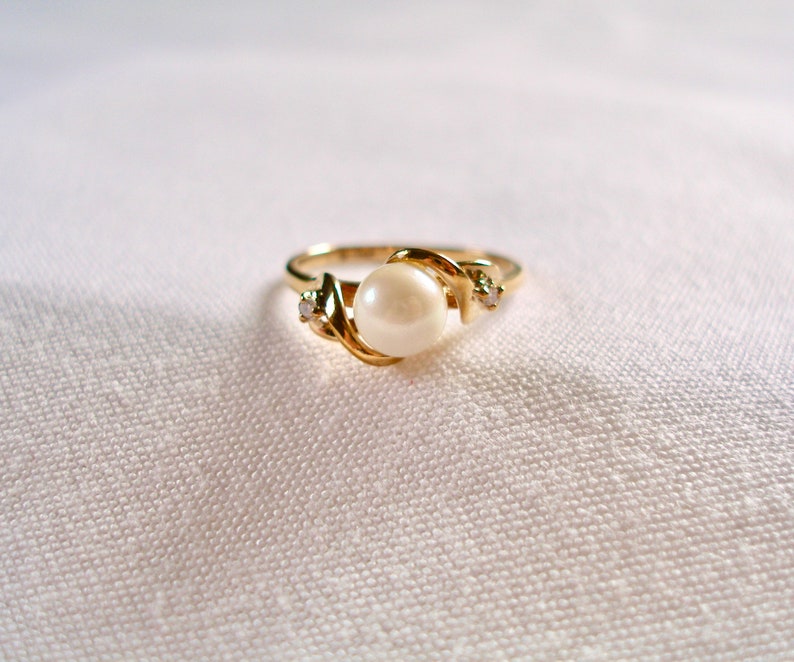 May include: A gold ring with a single pearl and two small diamonds. The ring is set in a twisted band.