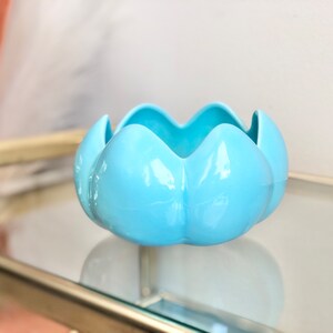 May include: A light blue ceramic bowl with a unique flower-like shape. The bowl has a glossy finish and is perfect for displaying small items or serving snacks.