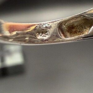 May include: Close-up of a silver ring with a hallmark stamp. The stamp reads "925". The ring's band is smooth and polished, reflecting the light. The ring is likely made of sterling silver.