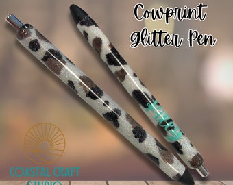 Puede incluir: Dos bolígrafos de purpurina con estampado de vaca con tapas negras. Los bolígrafos tienen una base blanca con manchas de vaca marrones y negras. El texto "Cowprint glitter Pen" está escrito en blanco y turquesa.