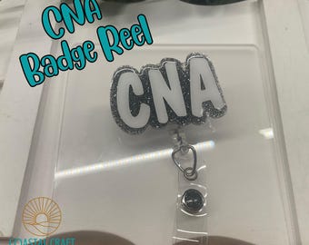 Puede incluir: Un carrete de insignia de brillo plateado con un dije blanco "CNA". El carrete está unido a un cordón retráctil de plástico transparente.