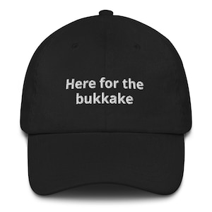 May include: Black baseball cap with white embroidered text that reads "Here for the bukkakake".