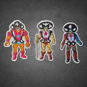 May include: Three embroidered patches featuring stylized figures wearing large black sombreros with white floral details. The figures are depicted in vibrant colors including red, orange, yellow, and blue, with one figure holding a long silver sword.